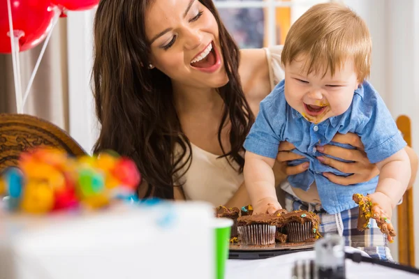 Mãe segurando menino com as mãos bagunçadas cobertas com bolo de gelo — Fotografia de Stock