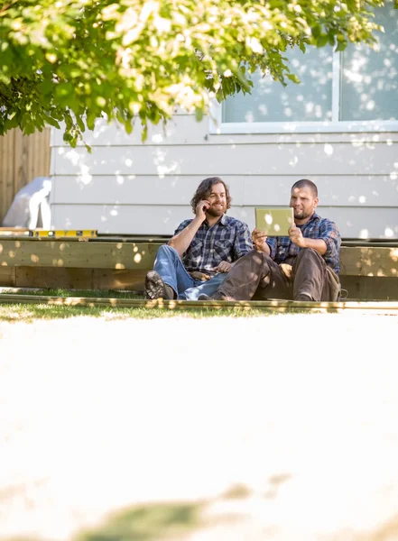 Carpenter Using Digital Tablet While Coworker On Call At Site — Stock Photo, Image