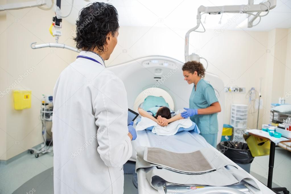 Doctor Looking At Nurse Preparing Patient For CT Scan