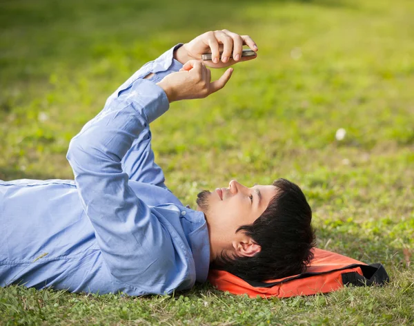 Άνθρωπος χρησιμοποιώντας mobilephone ενώ ξαπλωμένος στο γρασίδι στην πανεπιστημιούπολη — Φωτογραφία Αρχείου