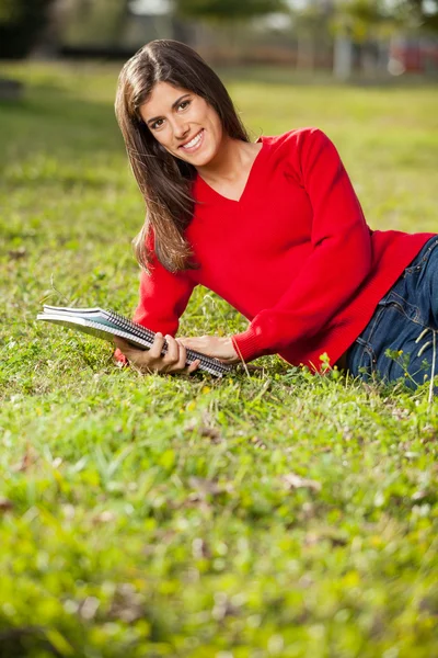 Mujer sosteniendo libros mientras se relaja en la hierba en el campus — Foto de Stock