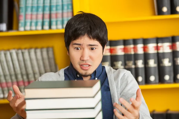 Studente guardando mucchio di libri nella biblioteca universitaria — Foto Stock