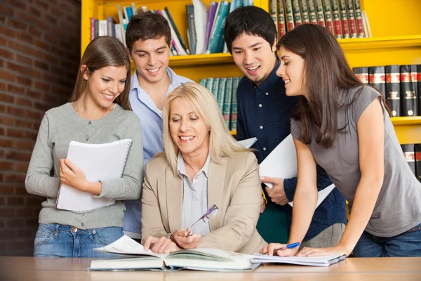 Lerares met boek uit te leggen van studenten in de bibliotheek — Stockfoto