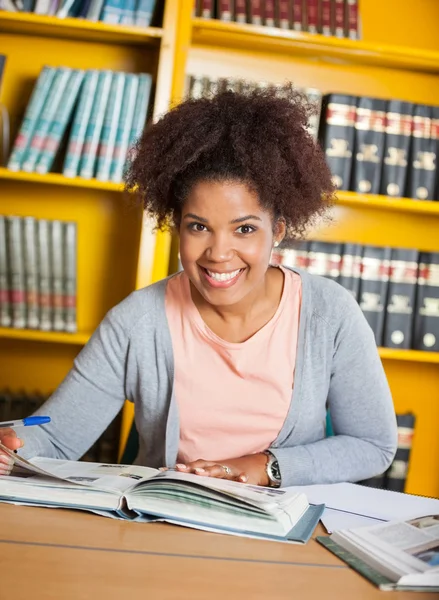 Estudante feminina com livros sentados na mesa na biblioteca — Fotografia de Stock