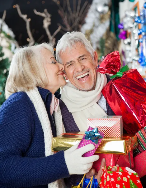 Frau küsst glücklichen Mann mit Weihnachtsgeschenken — Stockfoto