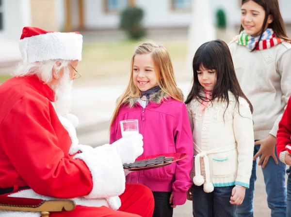 Santa claus erbjuder kakor och mjölk till barn — Stockfoto