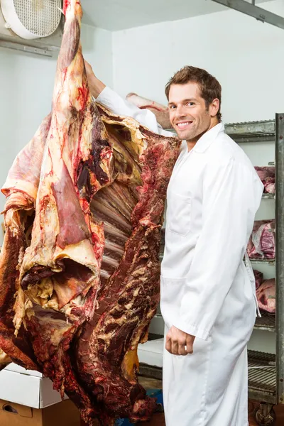 Açougueiro em pé no refrigerador com carne bovina — Fotografia de Stock