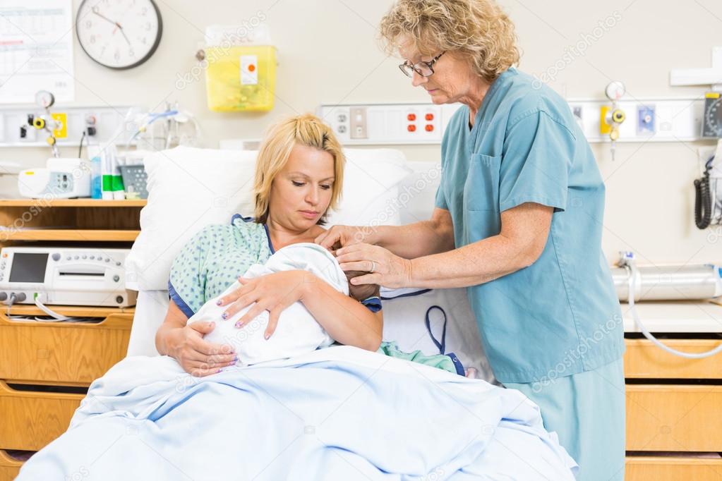Female Nurse Assisting Woman In Breast Feeding Baby In Hospital