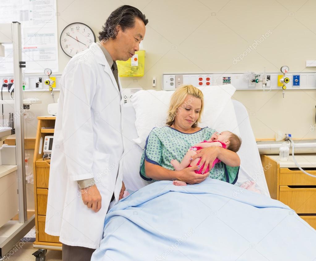Mother And Doctor Looking At Newborn Baby Girl In Hospital