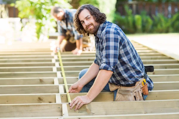 Carpintero midiendo madera con cinta mientras compañero de trabajo le ayuda — Foto de Stock