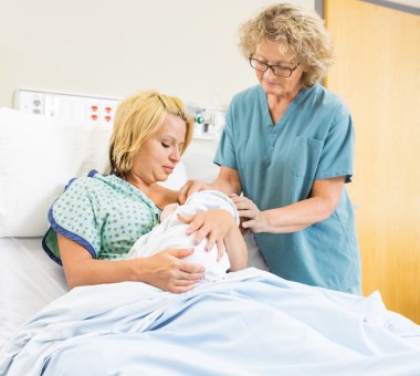 Nurse Assisting Woman In Breast Feeding Babygirl In Hospital clipart