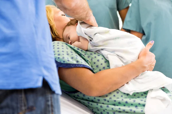 Babygirl couché sur la mère entourée d'infirmières et père — Photo