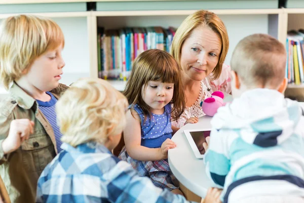 Lärare med elever som använder digital tablet i biblioteket — Stockfoto