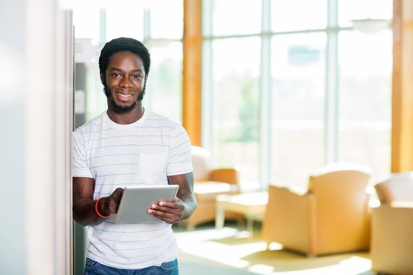 Student s digitálním tabletu stojící v knihovně — Stock fotografie