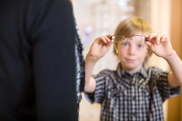 Niño sosteniendo gafas con la madre en primer plano en la tienda — Foto de Stock