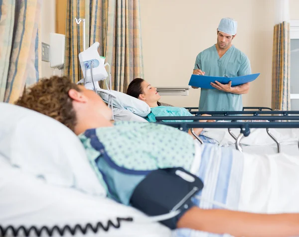 Paciente acostado en la cama mientras enfermera examina informe — Foto de Stock