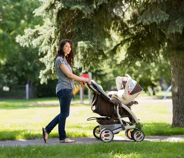 Giovane madre spingendo passeggino in parco — Foto Stock