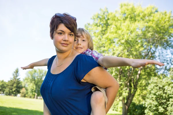 Mooie moeder met zoon op rug in het park — Stockfoto