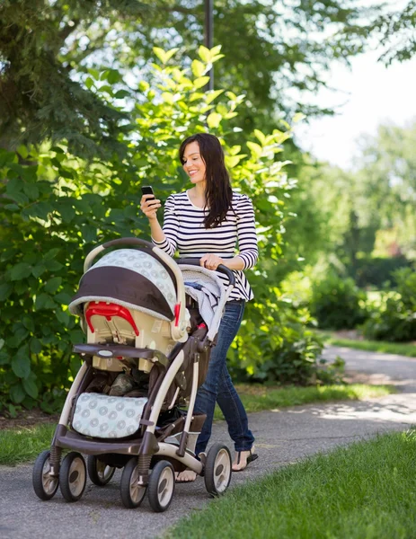 Kvinna med barnvagn med mobiltelefon i parken — Stockfoto