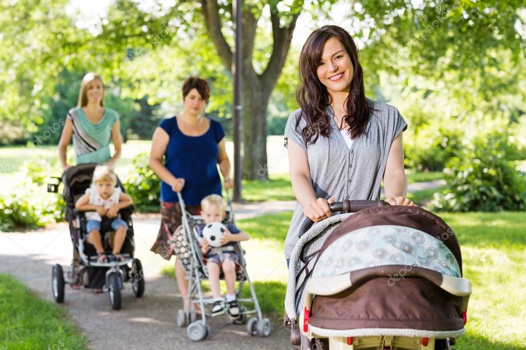 Beautiful Mother Pushing Baby Stroller In Park Stock Photo by