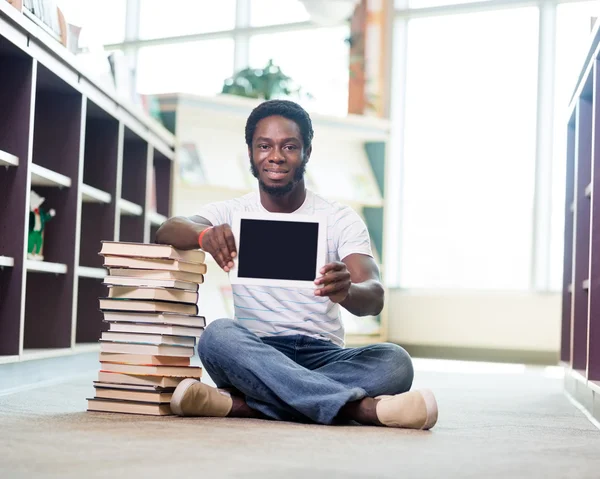 Student s knihami ukazující digitálním tabletu v knihovně — Stock fotografie