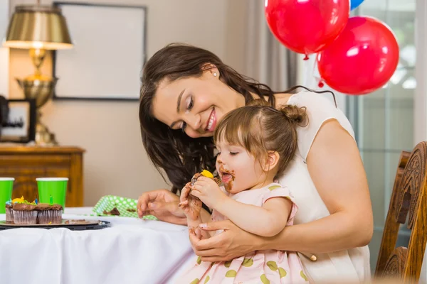 Mãe olhando para aniversário menina comer bolo — Fotografia de Stock