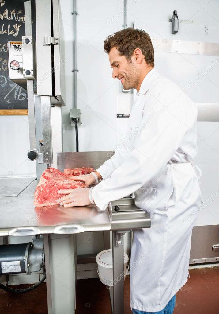 Smiling Butcher Slicing Meat On Bandsaw
