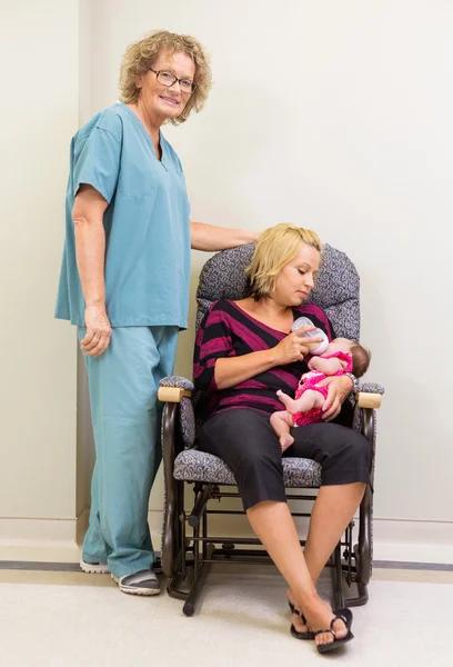 Enfermera de pie junto a la madre alimentando a la recién nacida en el hospital —  Fotos de Stock