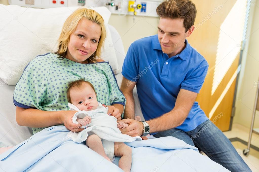 Woman With Newborn Baby Girl Sitting By Man In Hospital