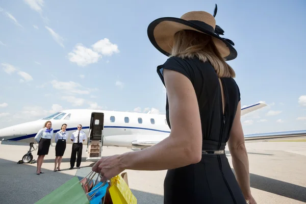 Богатая женщина с мешками для покупок идет к частному самолету — стоковое фото