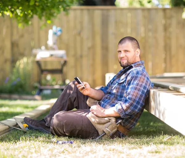 Confident Carpenter Messaging On Cellphone While Leaning On Wood — Stock Photo, Image