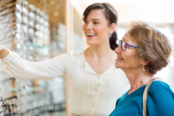 Kobieta pomoc starszych klient wybierając okulary — Zdjęcie stockowe