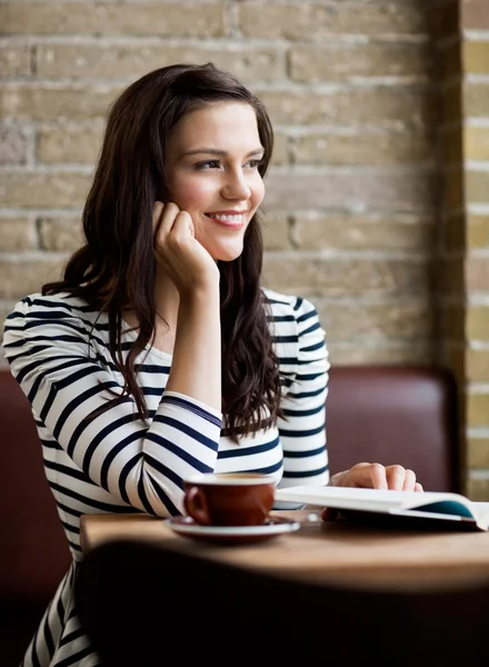 Женщина с рукой на подбородке смотрит в сторону в кафе — стоковое фото