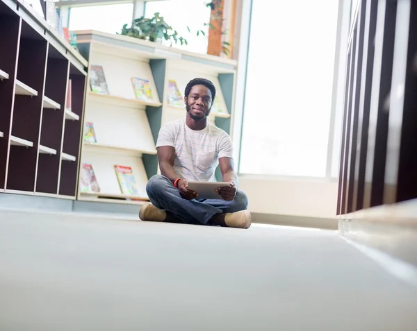 Studente maschio con tavoletta digitale seduto in biblioteca — Foto Stock