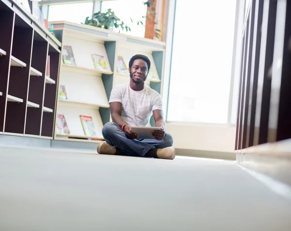 Étudiant mâle avec tablette numérique assis dans la bibliothèque — Photo