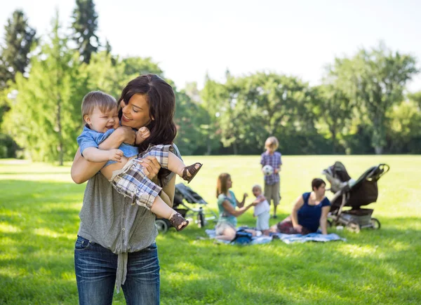 Jeune femme portant un bébé garçon dans le parc — Photo