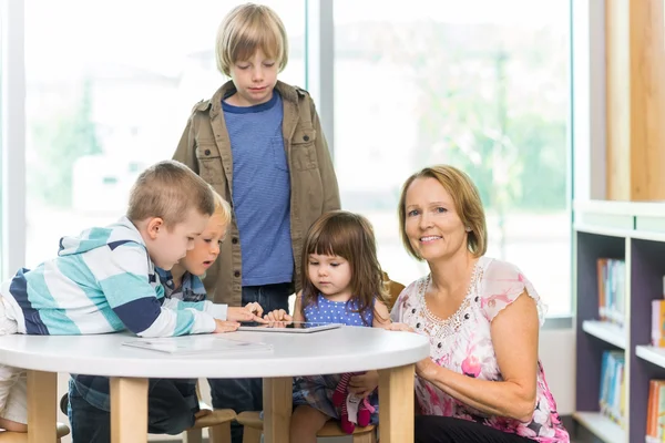 Lehrer mit Schülern, die Tablet-Computer in der Bibliothek benutzen — Stockfoto