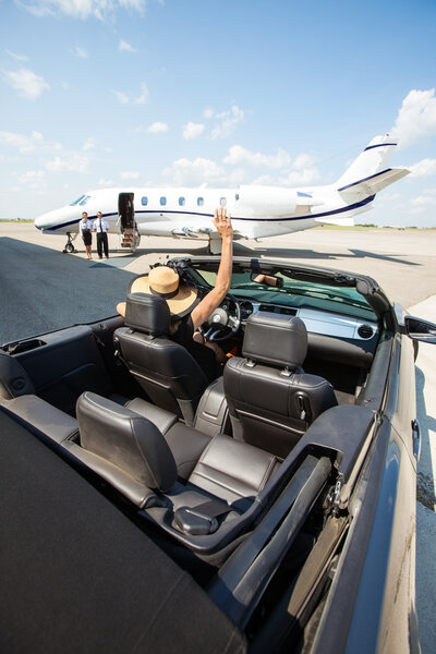 Woman In Convertible Waving To Pilot And Stewardess Against Jet