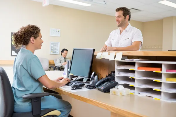 Krankenschwester und Patient im Gespräch an der Rezeption Stockbild