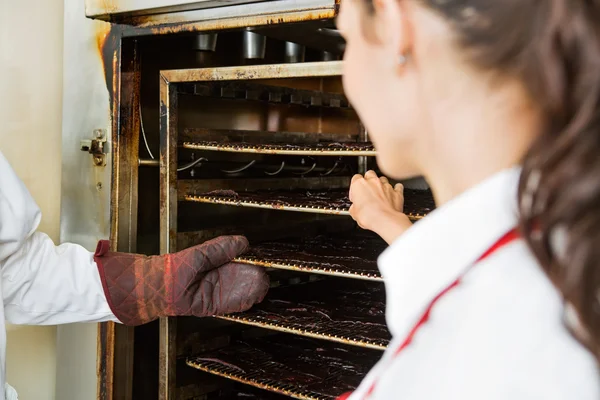 Trabajadores eliminando rebanadas de carne seca del horno en la tienda —  Fotos de Stock