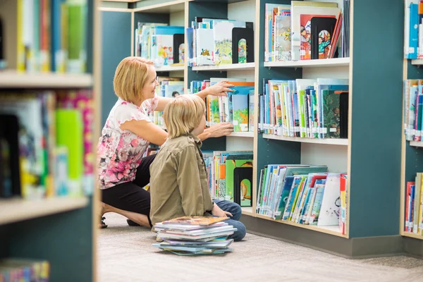 Lärare hjälpa pojken vid valet av böcker i biblioteket — Stockfoto