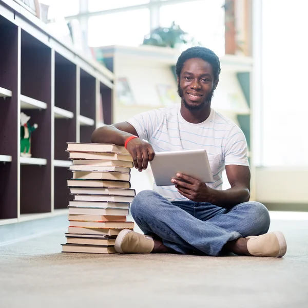 Student z książek i cyfrowy tablicowy siedzi w bibliotece — Zdjęcie stockowe