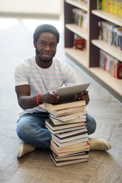 Студент с книгами и цифровыми планшетами сидит в библиотеке — стоковое фото