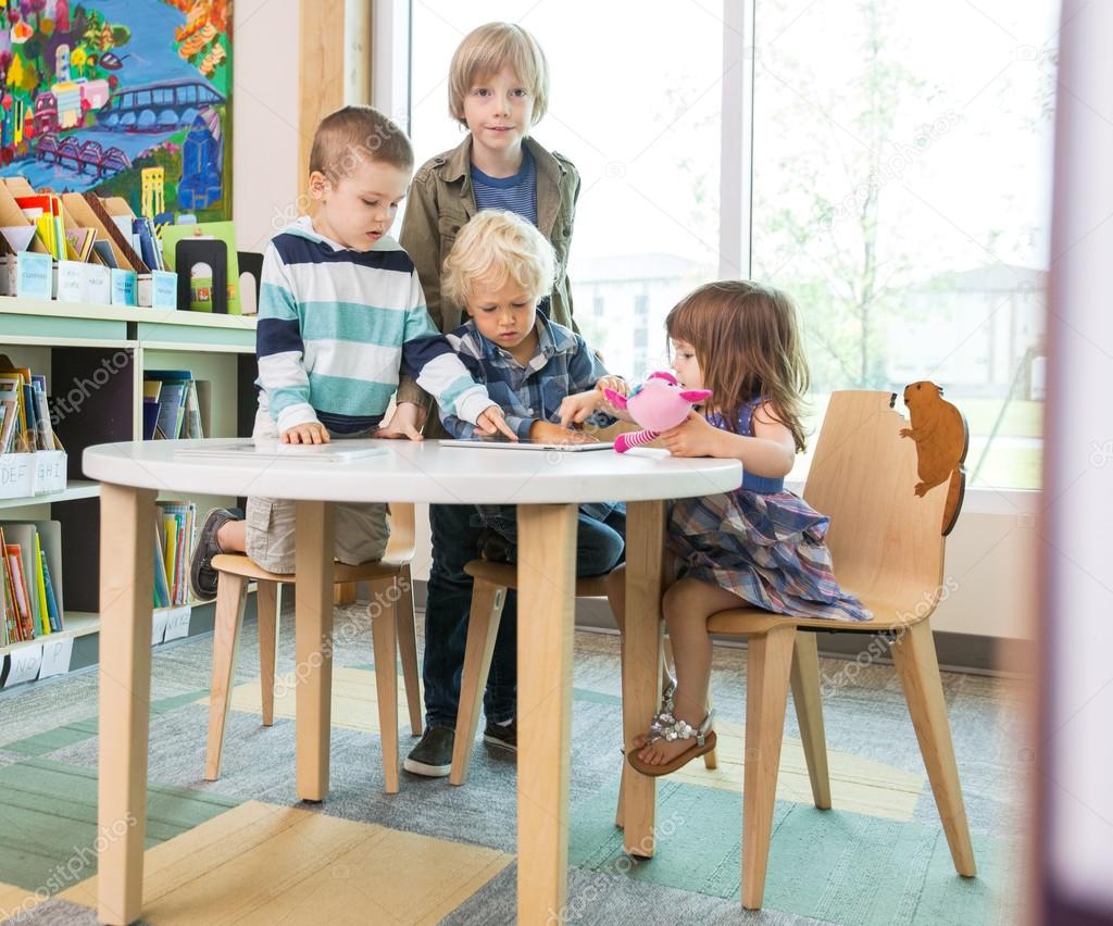 Children Using Digital Tablet At Table In Library