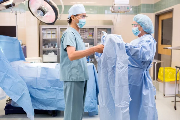 Skrubba sjuksköterska hjälper kirurgen med klänning — Stockfoto