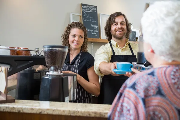 Vlastníci Café podává kávu k ženě u přepážky — Stock fotografie