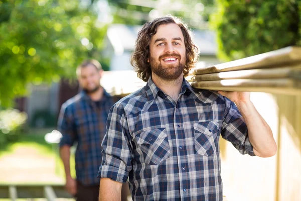 Gelukkig Carpenter met collega uitvoering planken buitenshuis — Stockfoto