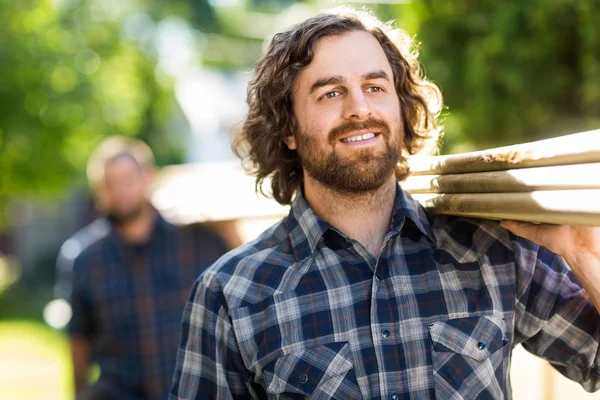 Carpenter Smiling While Carrying Planks With The Help Of Coworke — Stock Photo, Image