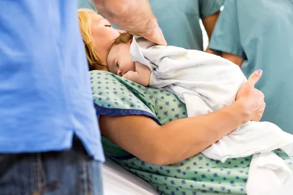 Babygirl couché sur la mère entourée d'infirmières et père — Photo