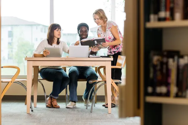 Studenten en bibliothecaris kijken naar boeken in bibliotheek — Stockfoto